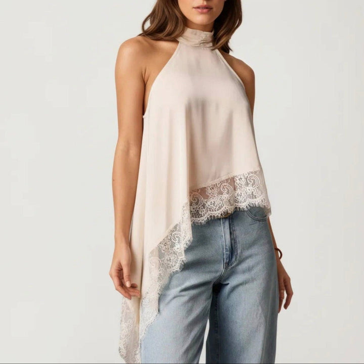 A woman wearing a sleeveless high-neck halter top in a light cream or beige color with a lace trim along the hem, paired with light-wash blue jeans, against a plain light gray background.